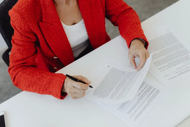 A business owner signs paperwork with a pen at her desk