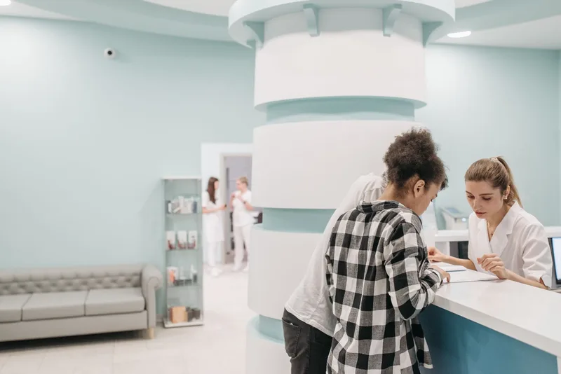 Staff assist a patient at a clinic reception desk