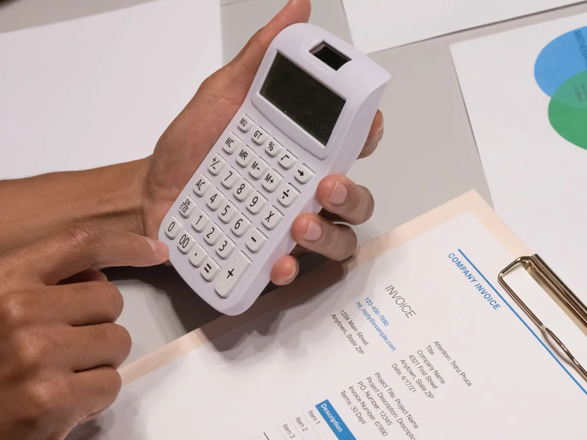 Close-up of hands using a calculator next to an invoice