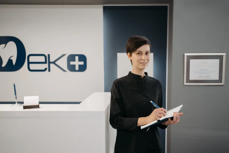 Dental clinic receptionist holding a notebook and pen at the front desk